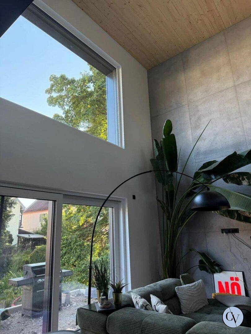Helles Wohnzimmer mit hohen Fenstern, Blick ins Grüne und Zugang zum Gartenbereich.