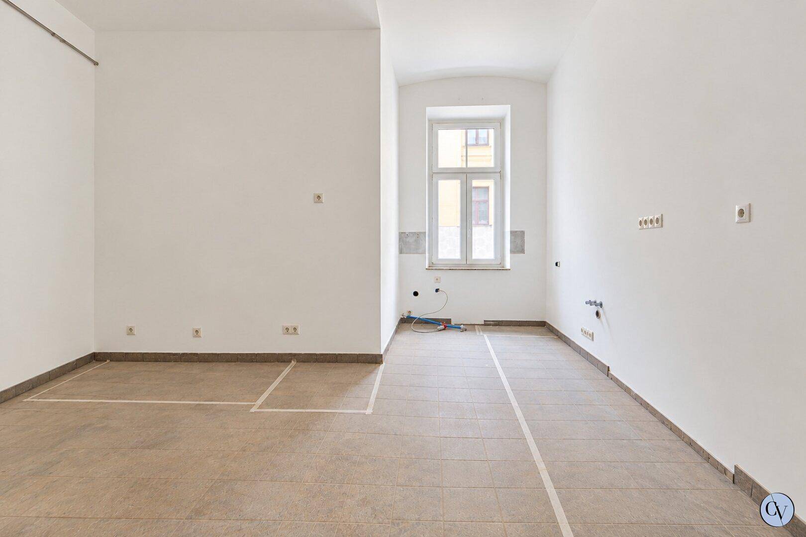 Heller, leerer Raum mit weiß gestrichenen Wänden, einem Fenster und Fliesenboden.