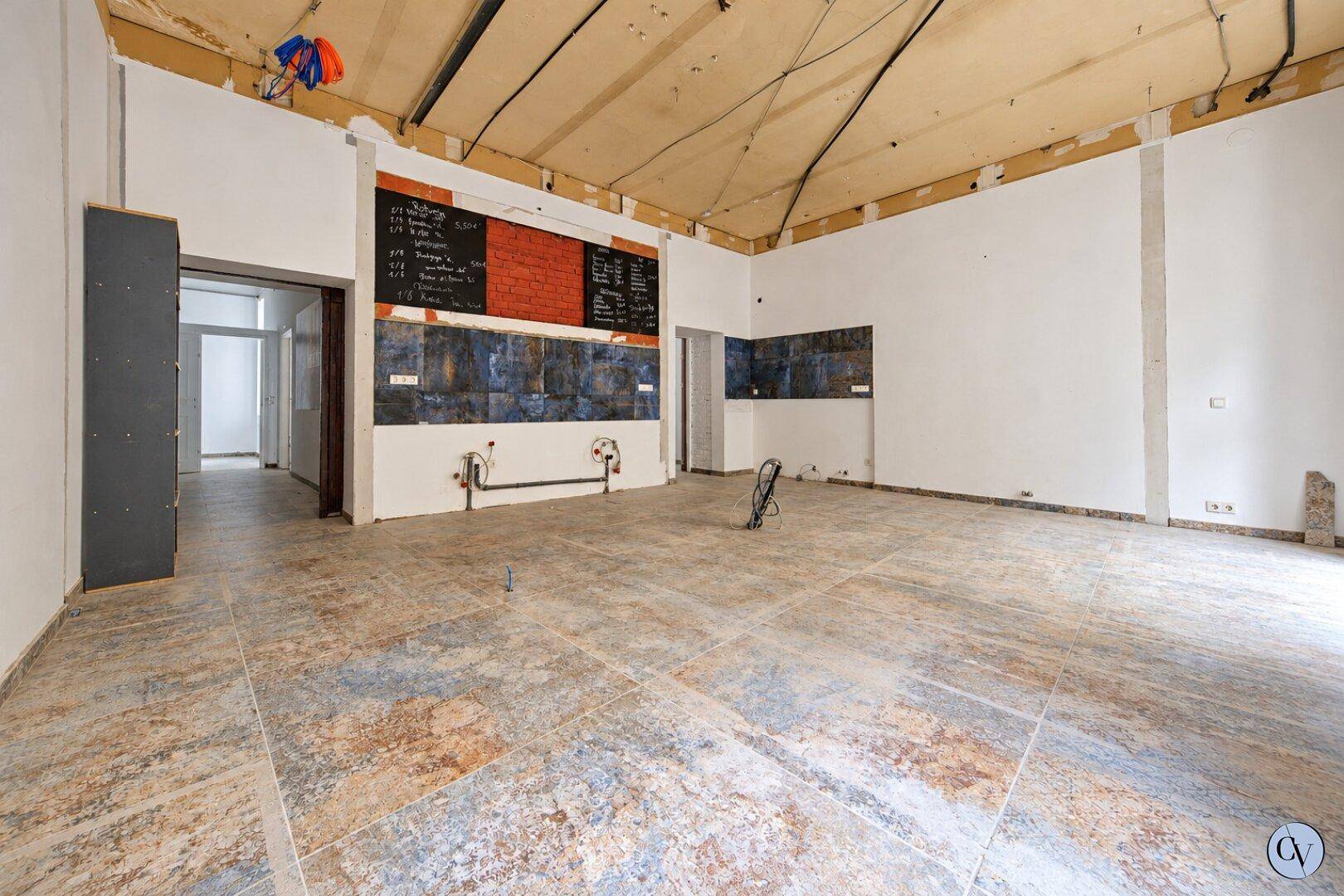 Geräumiger Innenraum im Rohbau mit Fliesenboden, vorbereiteten Wänden und sichtbaren Installationen.