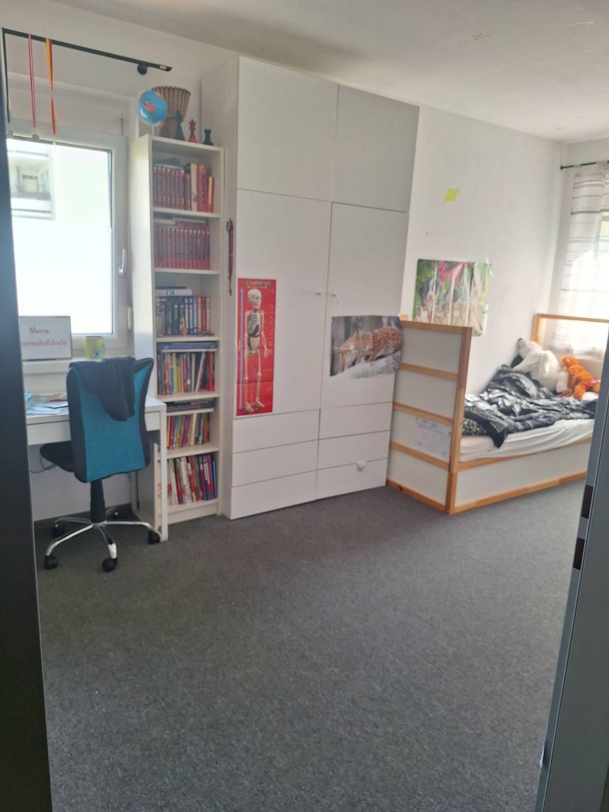Geräumiges Kinderzimmer mit Schreibtisch, Bücherregal, weißem Kleiderschrank und Teppichboden.