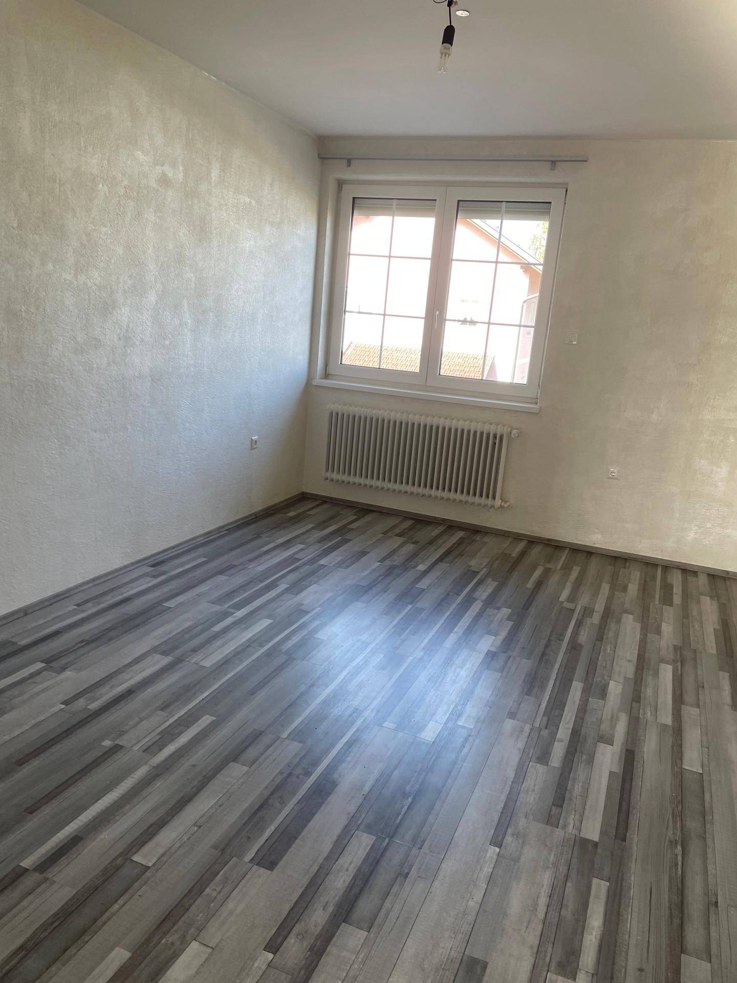 Helles Schlafzimmer mit strukturierten Wänden, Laminatboden und Fenster.