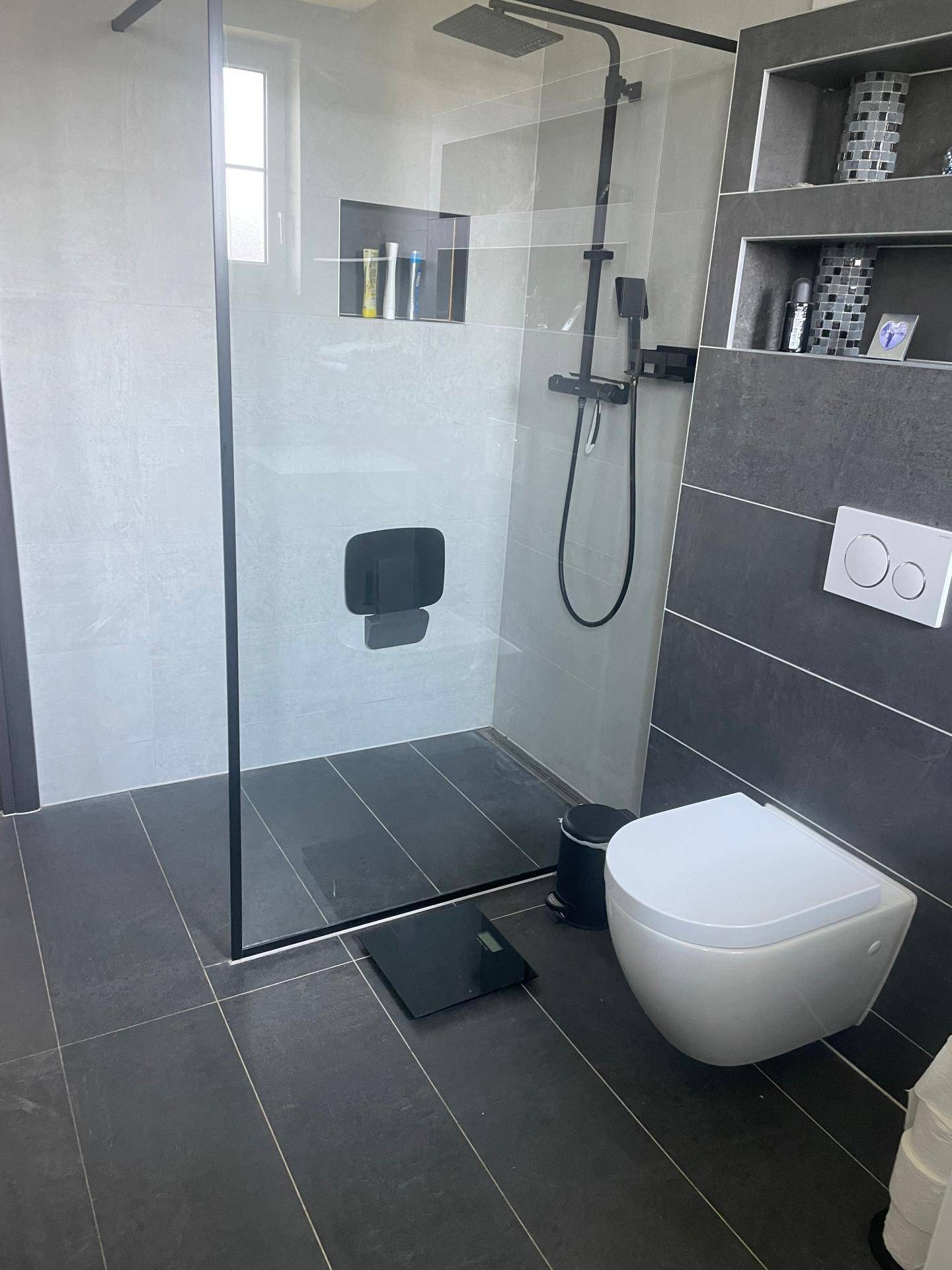 Modernes Badezimmer mit dunklen Fliesen, begehbarer Dusche und wandhängendem WC.