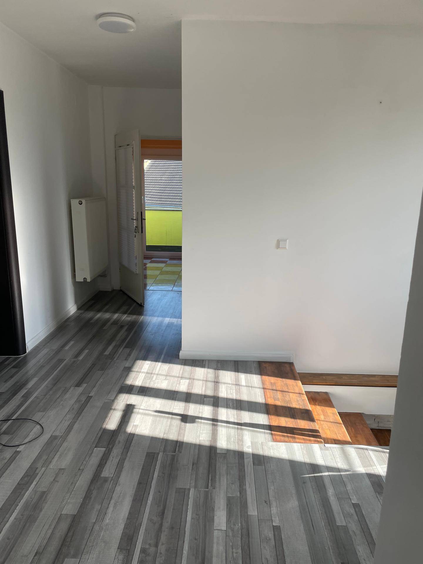 Heller Flur mit Laminatboden, Treppe und Zugang zu einem Außenbereich.