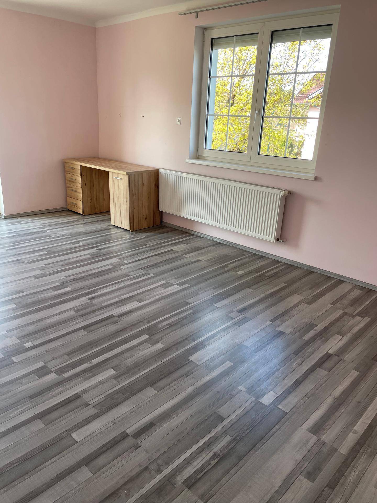 Schlafzimmer mit rosa Wänden, Laminatboden, Holzschreibtisch und großem Fenster.