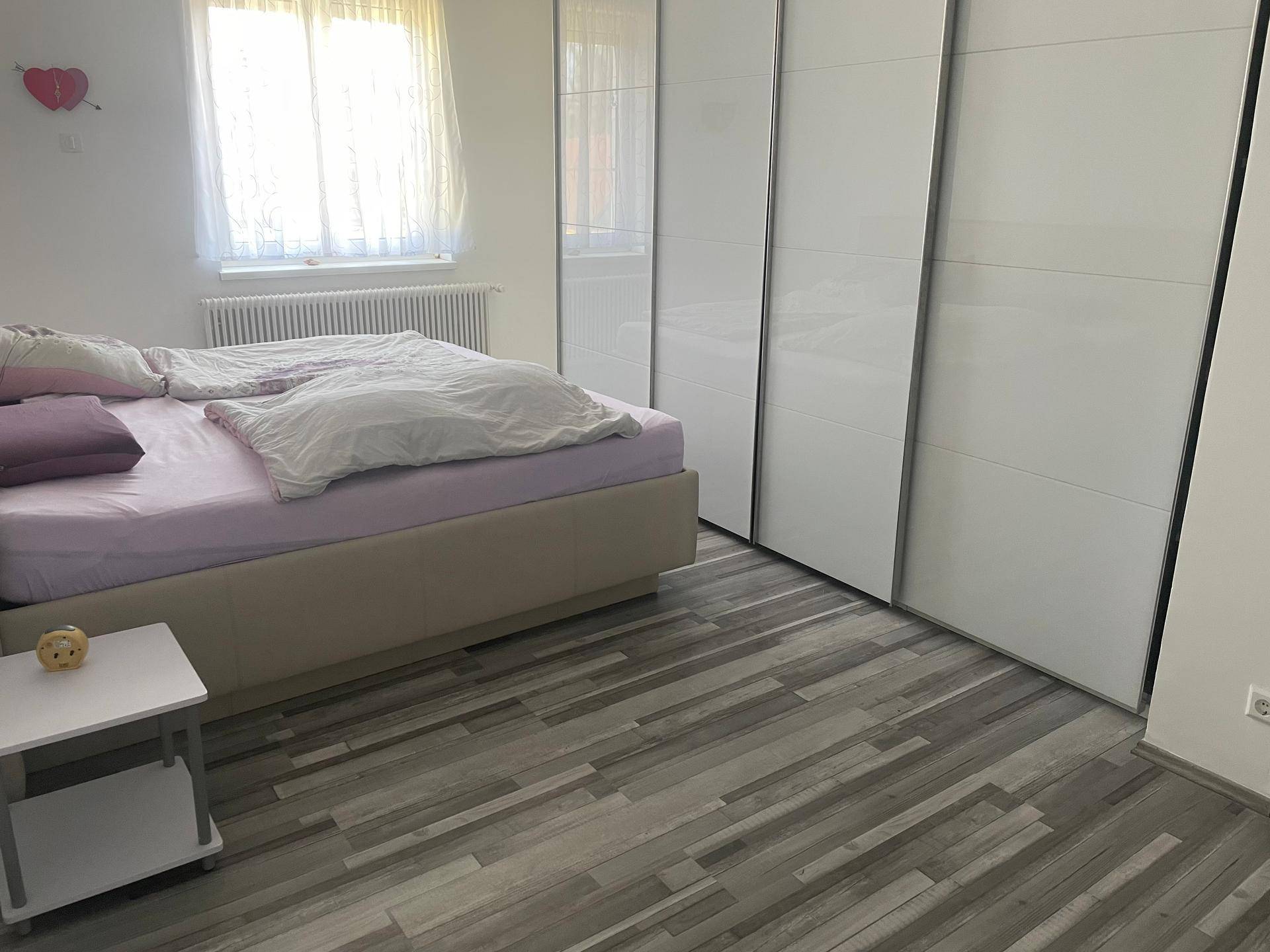 Helles Schlafzimmer mit modernem Bett, weißen Einbauschränken und Laminatboden für gemütliche Nächte.