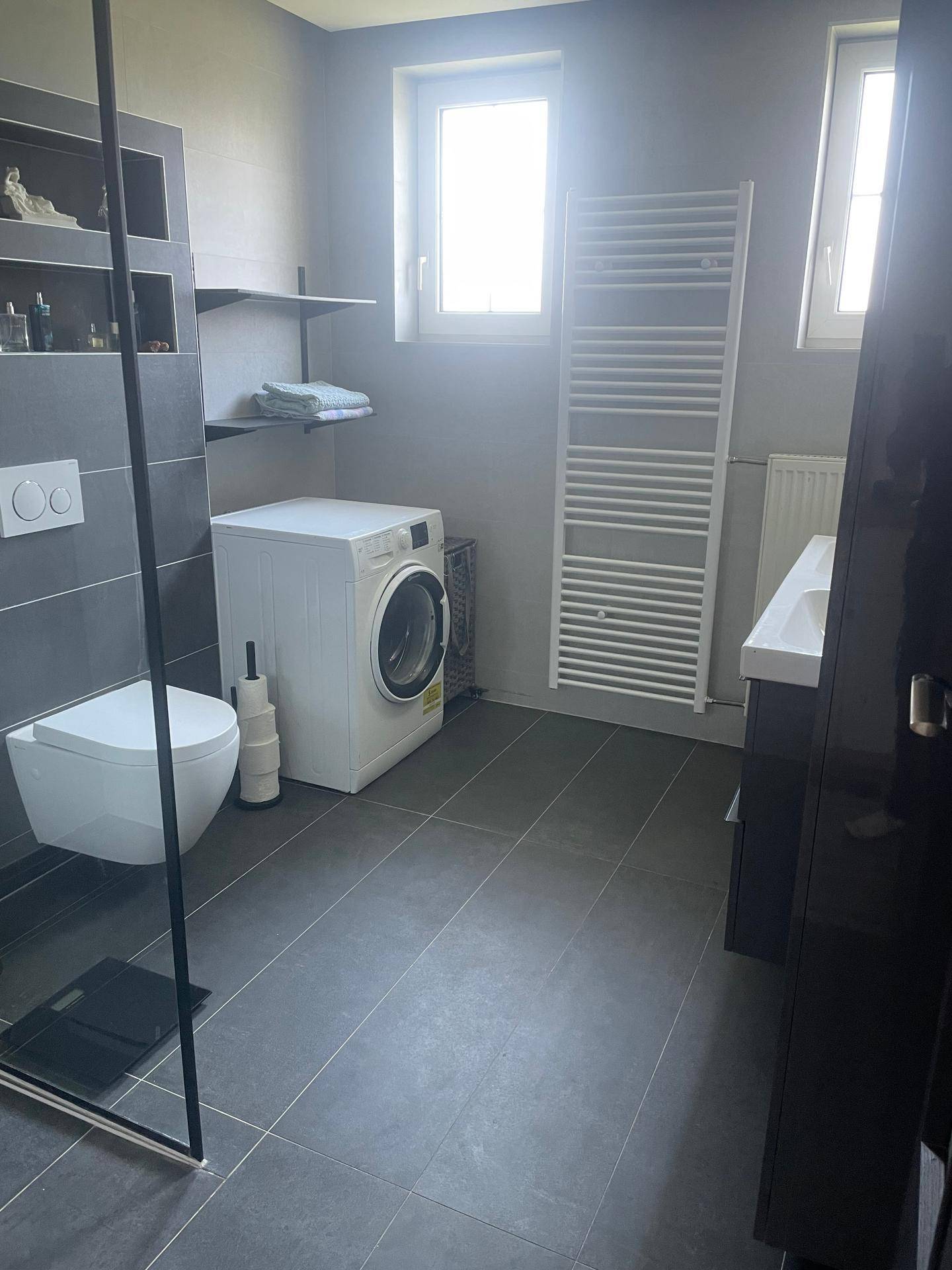 Modernes Badezimmer mit begehbarer Dusche, wandhängendem WC, Fenster und beheiztem Handtuchhalter.