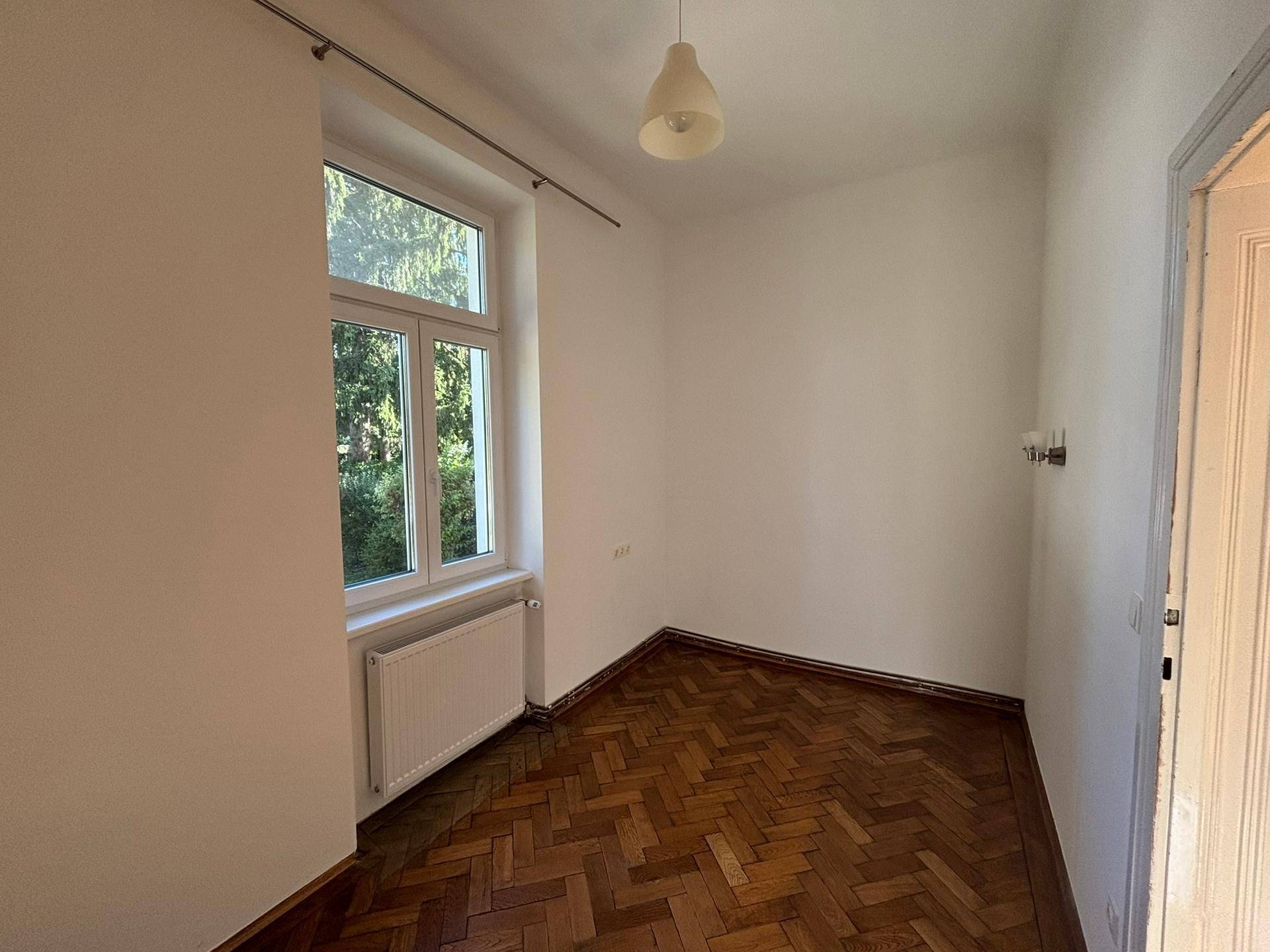 Gemütliches Zimmer mit Fischgrätparkett und einem Fenster, das viel Tageslicht hereinlässt.