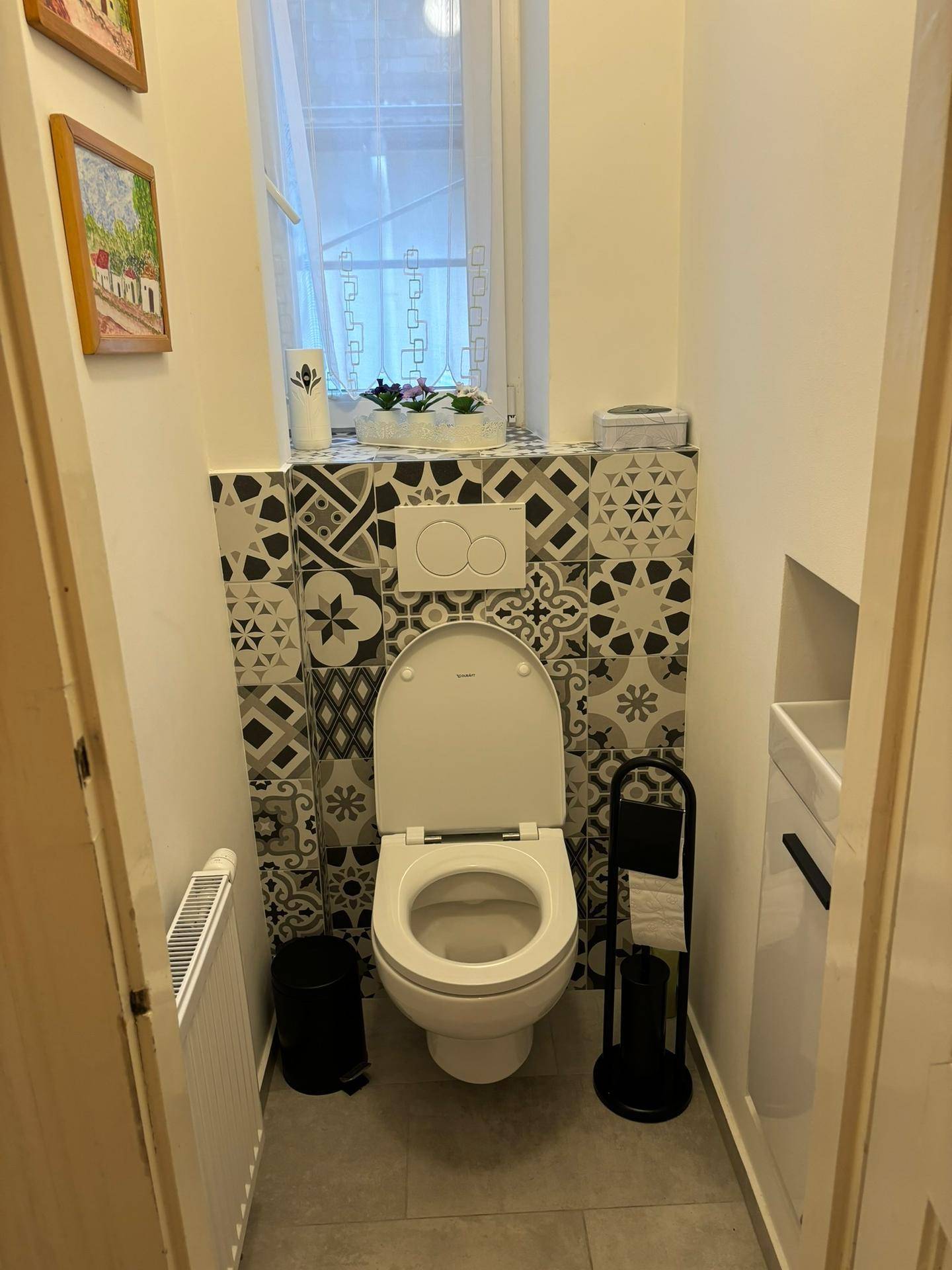 Gäste-WC mit dekorativen Fliesen, wandhängender Toilette und einem Fenster für Tageslicht.