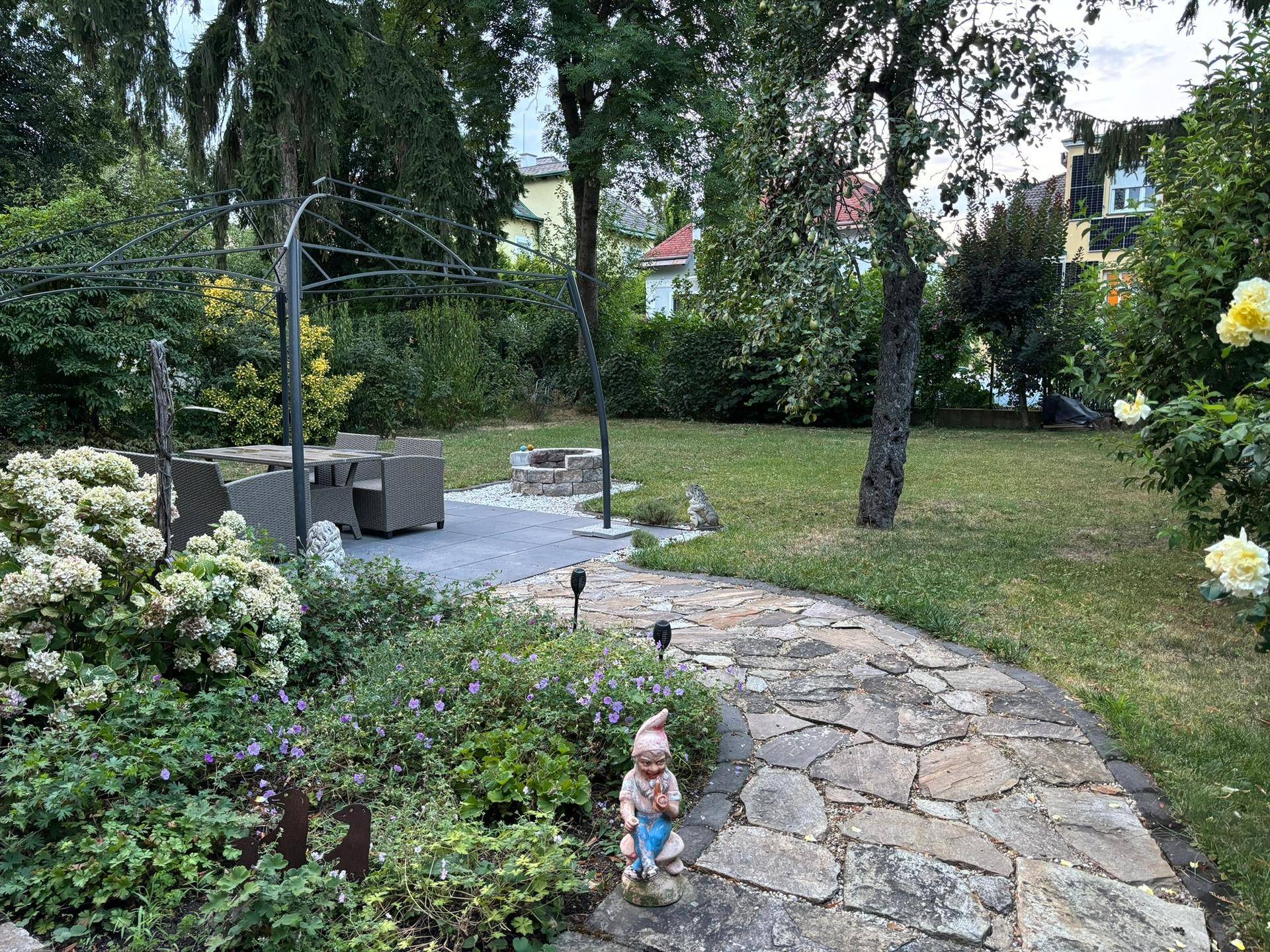 Idyllischer Garten mit Steinweg, blühenden Pflanzen und einem Gartenzwerg als Dekoration.
