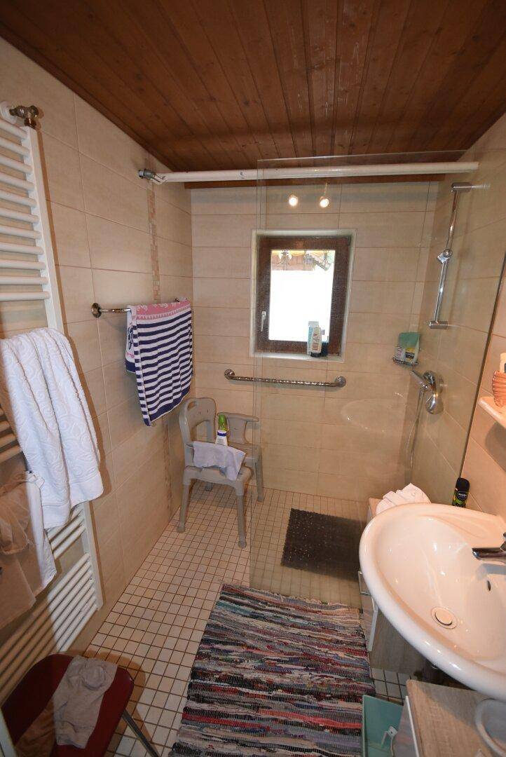 Helles Badezimmer mit Dusche, Fliesenboden und Holzdecke.