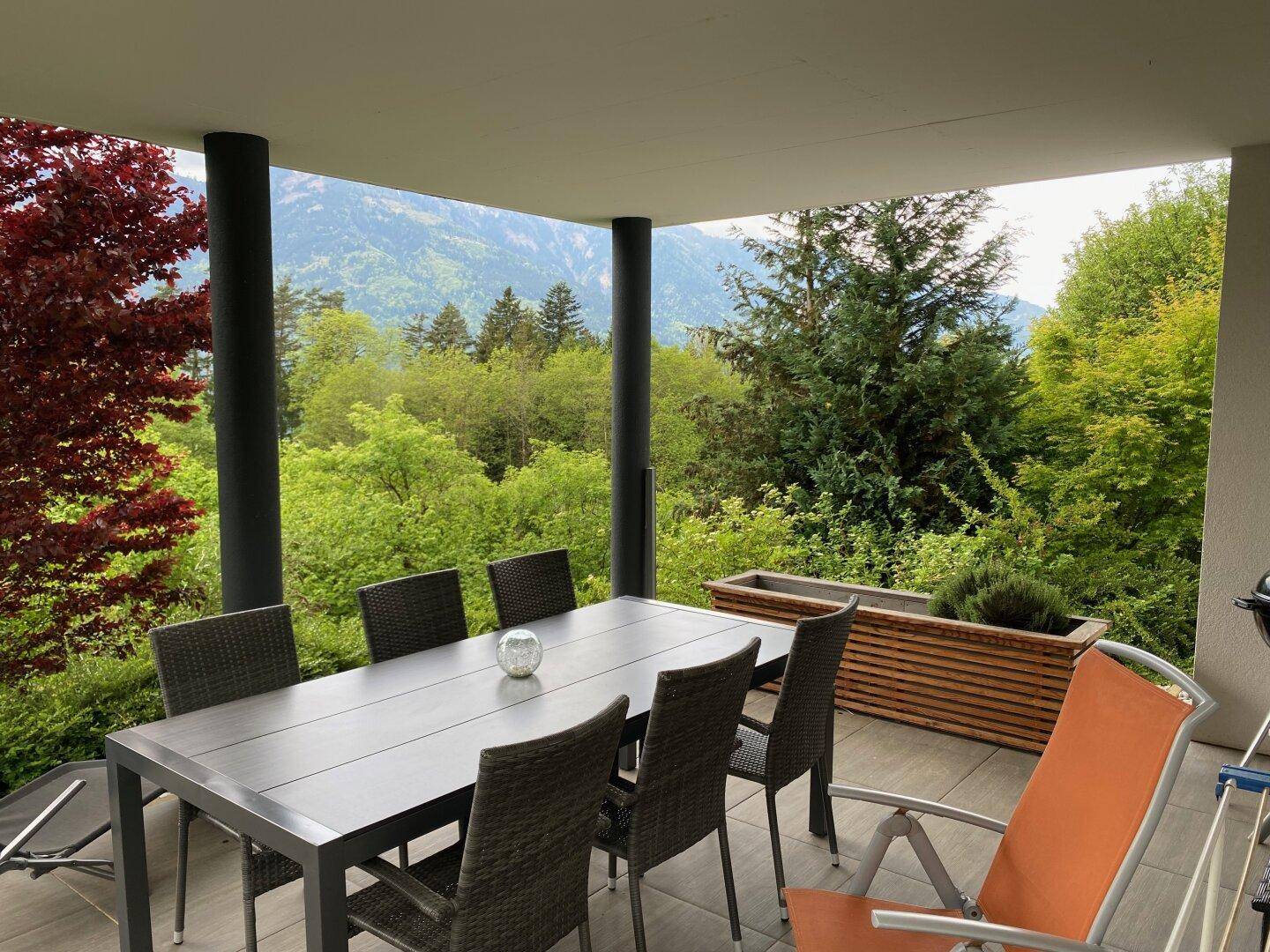 Überdachte Terrasse mit Esstisch und Stühlen, bietet einen weiten Blick auf die Berge.
