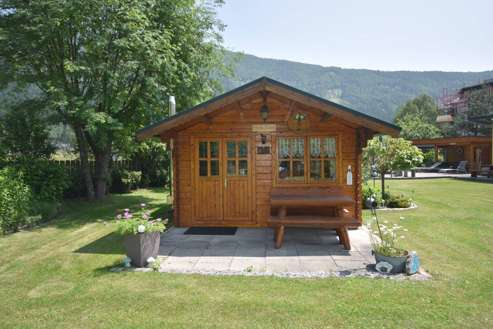 Charmantes Holzgartenhaus mit Sitzbank, umgeben von Grünflächen und Bergblick.