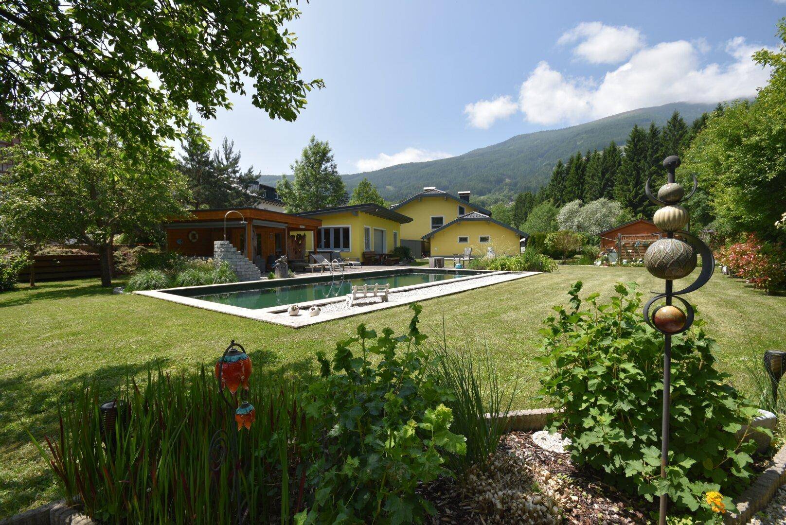 Weitläufiger Garten mit großem Pool, gelbem Haus und beeindruckendem Bergpanorama.