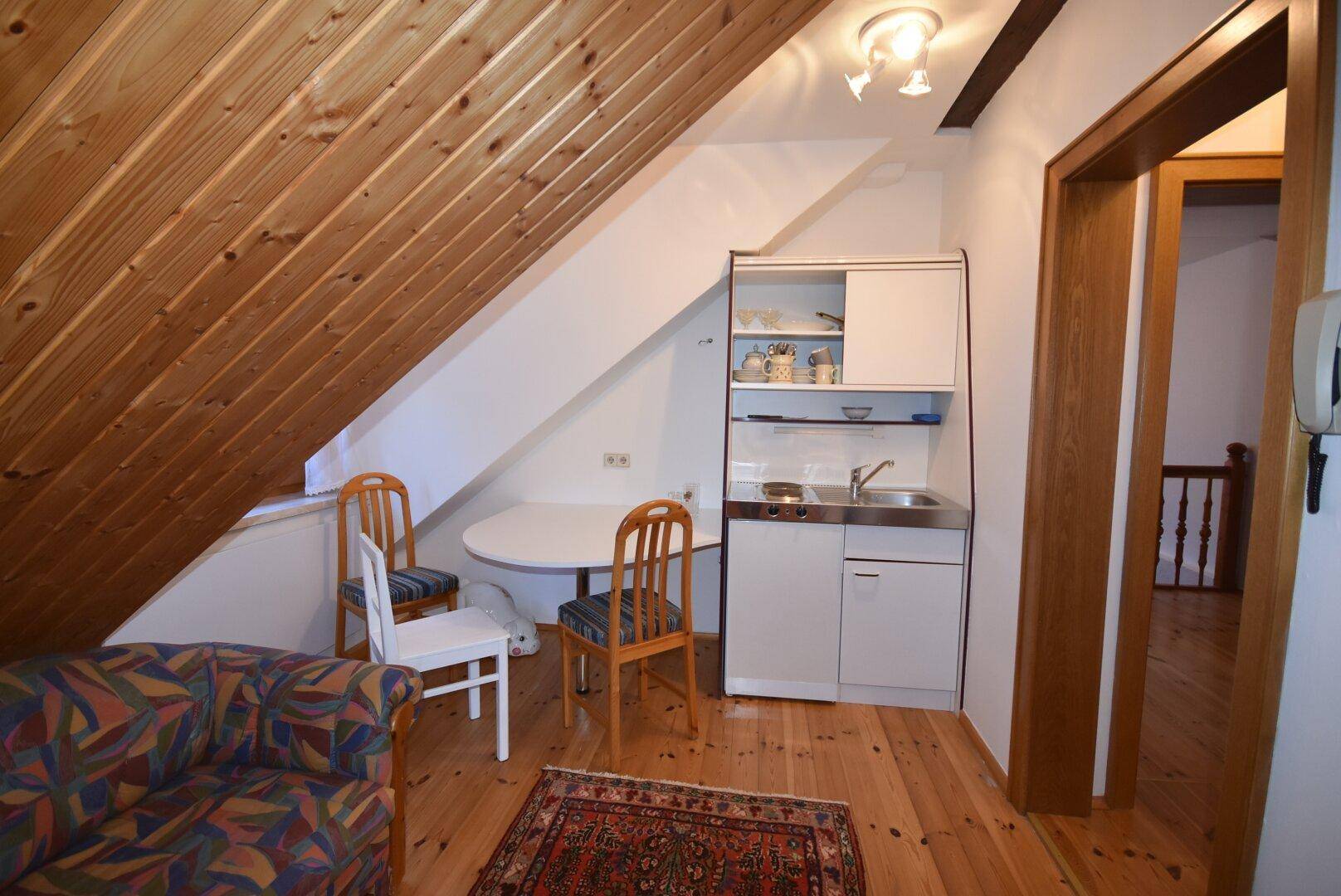 Gemütlicher Dachraum mit Holzverkleidung, kleiner Küchenzeile und Sitzgelegenheiten.