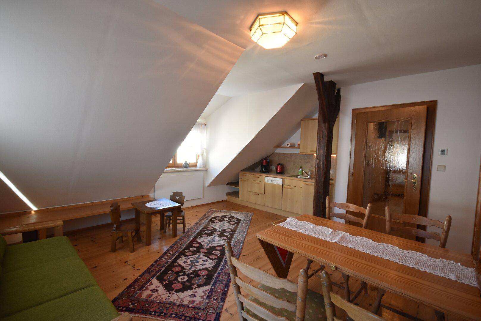 Helles Dachzimmer mit Holzboden, Essbereich und integrierter Küchenzeile unter der Dachschräge.