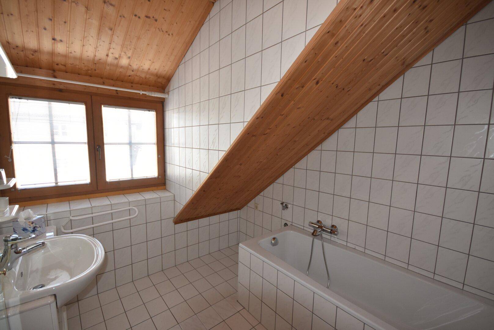 Gefliestes Badezimmer im Dachgeschoss mit Badewanne, Waschbecken und Holzdecke.