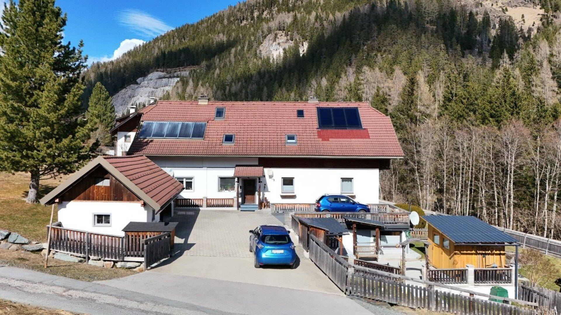 Großes Einfamilienhaus mit Photovoltaikanlage auf dem Dach und zwei Autos in der Einfahrt.