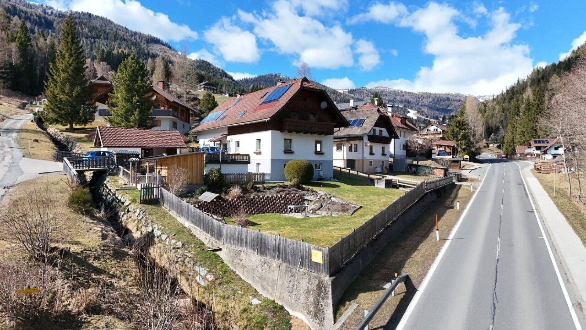 Weitläufige Ansicht des Hauses in einer Berglandschaft mit Straße und Nachbargebäuden.