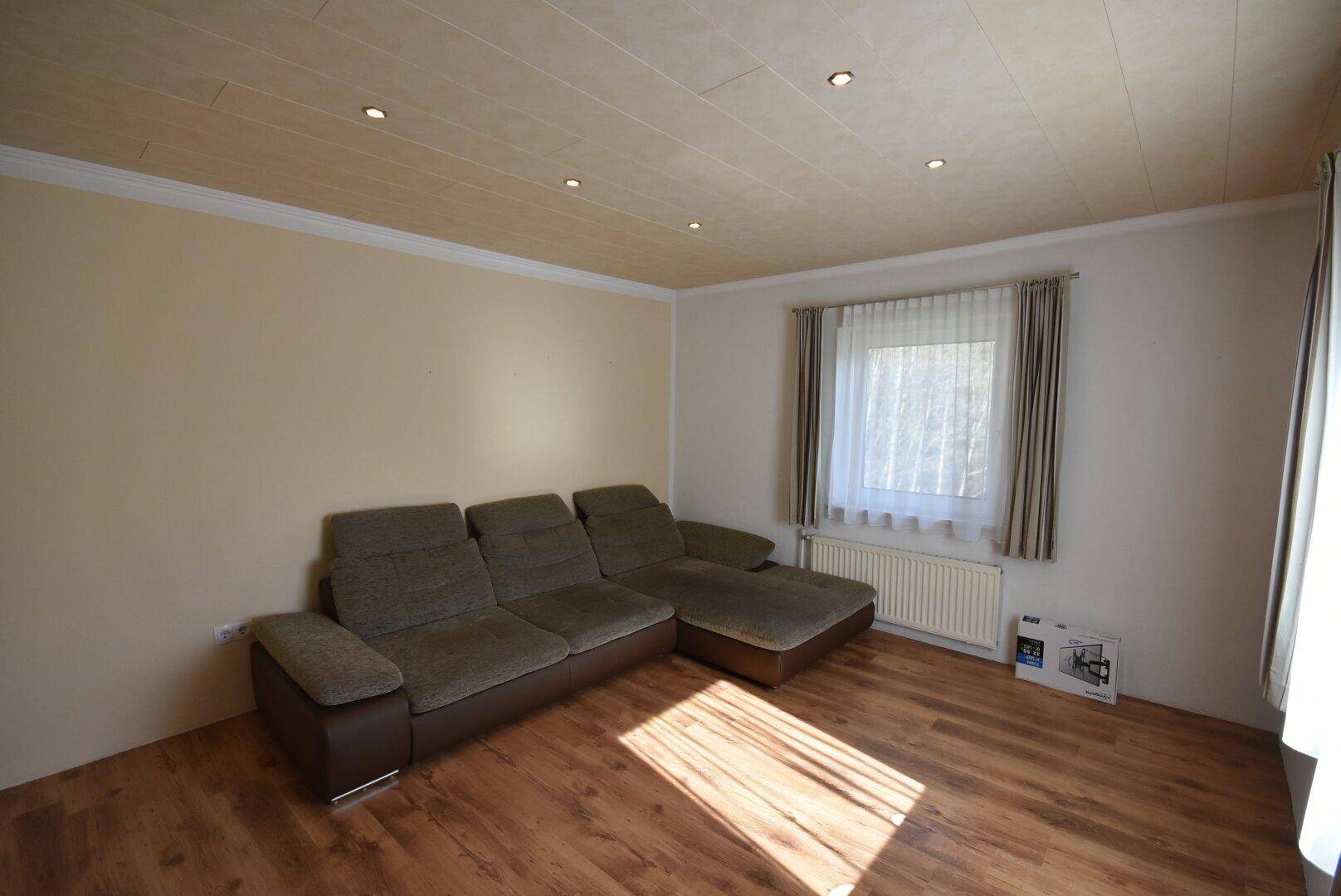 Helles Wohnzimmer mit beigem Sofa, Holzdecke und Laminatboden.