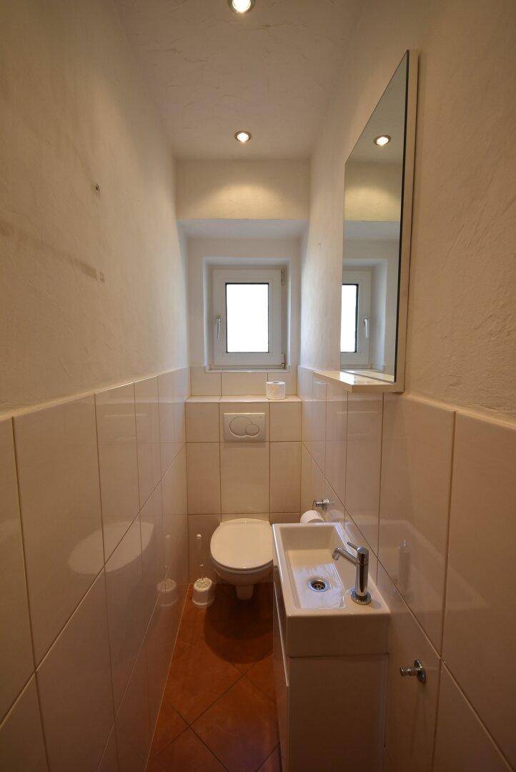 Kleines Gäste-WC mit Waschbecken, Toilette und Fenster.