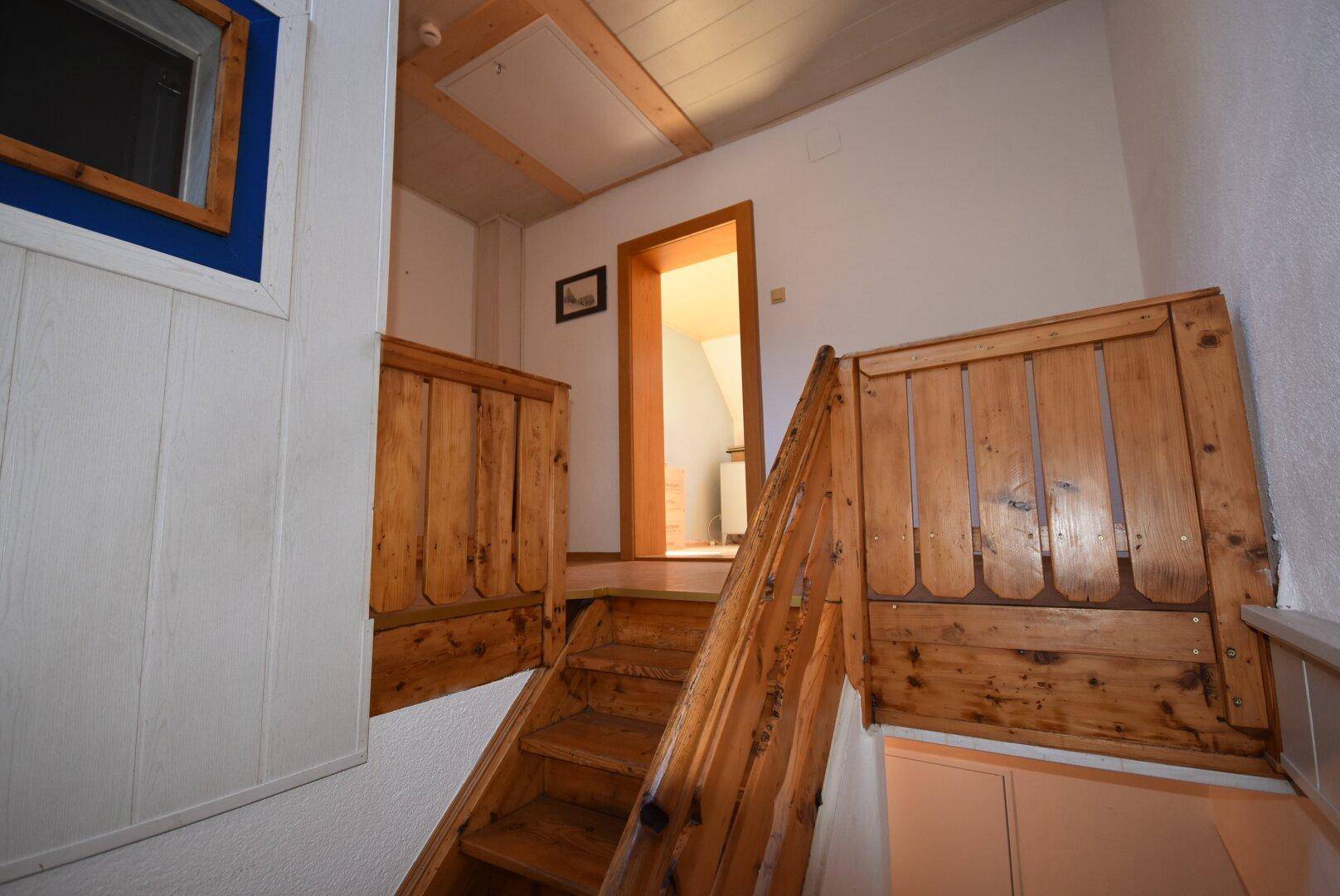 Holztreppe im Flur mit rustikalem Geländer und Zugang zu weiteren Räumen.