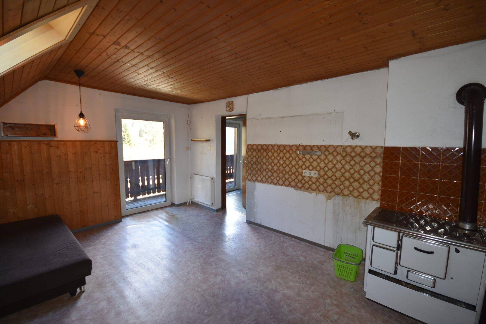 Rustikaler Wohnraum mit Holzdecke, traditionellem Ofen und Balkonzugang.