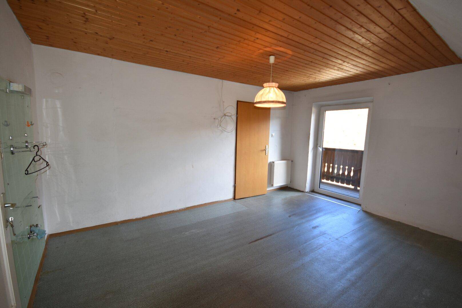 Schlafzimmer mit Holzdecke, Balkonzugang und einfacher Ausstattung.