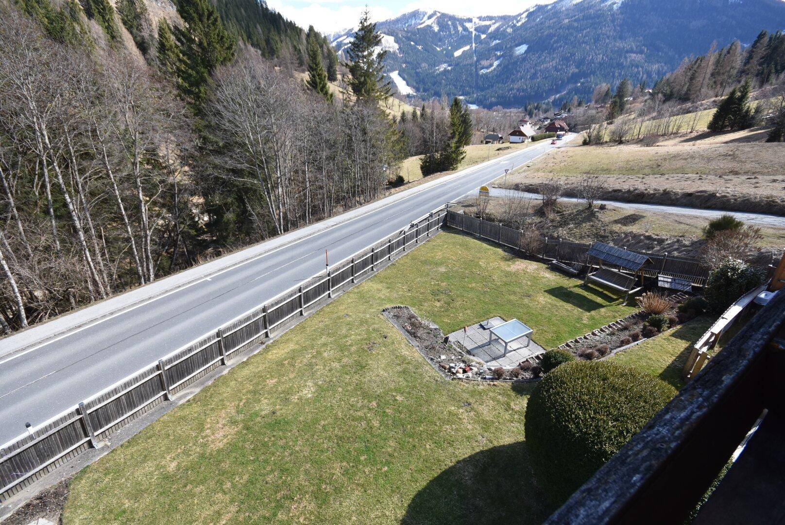 Gartenbereich mit Rasenfläche, Sitzgelegenheiten und Blick auf die Straße und Berge.