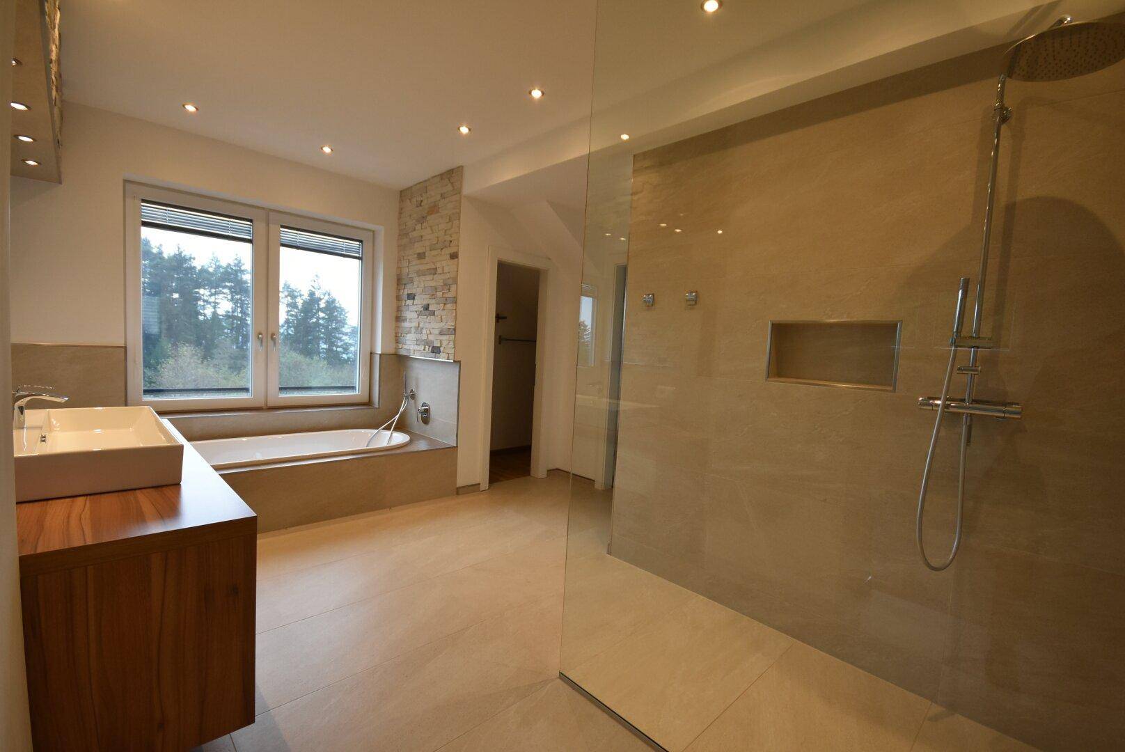 Modernes Badezimmer mit großer Dusche, Badewanne und Fenster mit Waldblick.