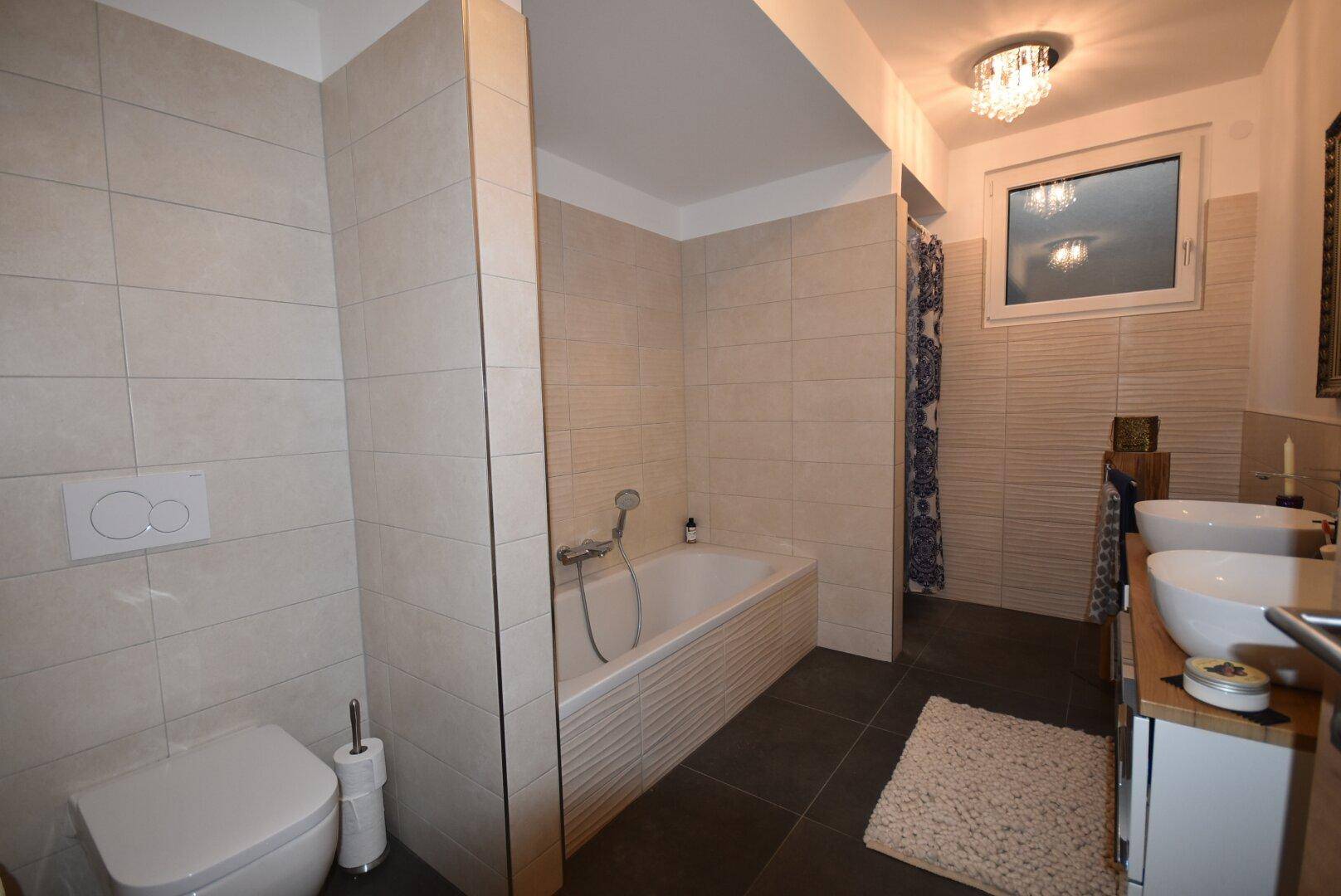 Modernes Badezimmer mit Badewanne, Doppelwaschbecken und hellen Fliesen.
