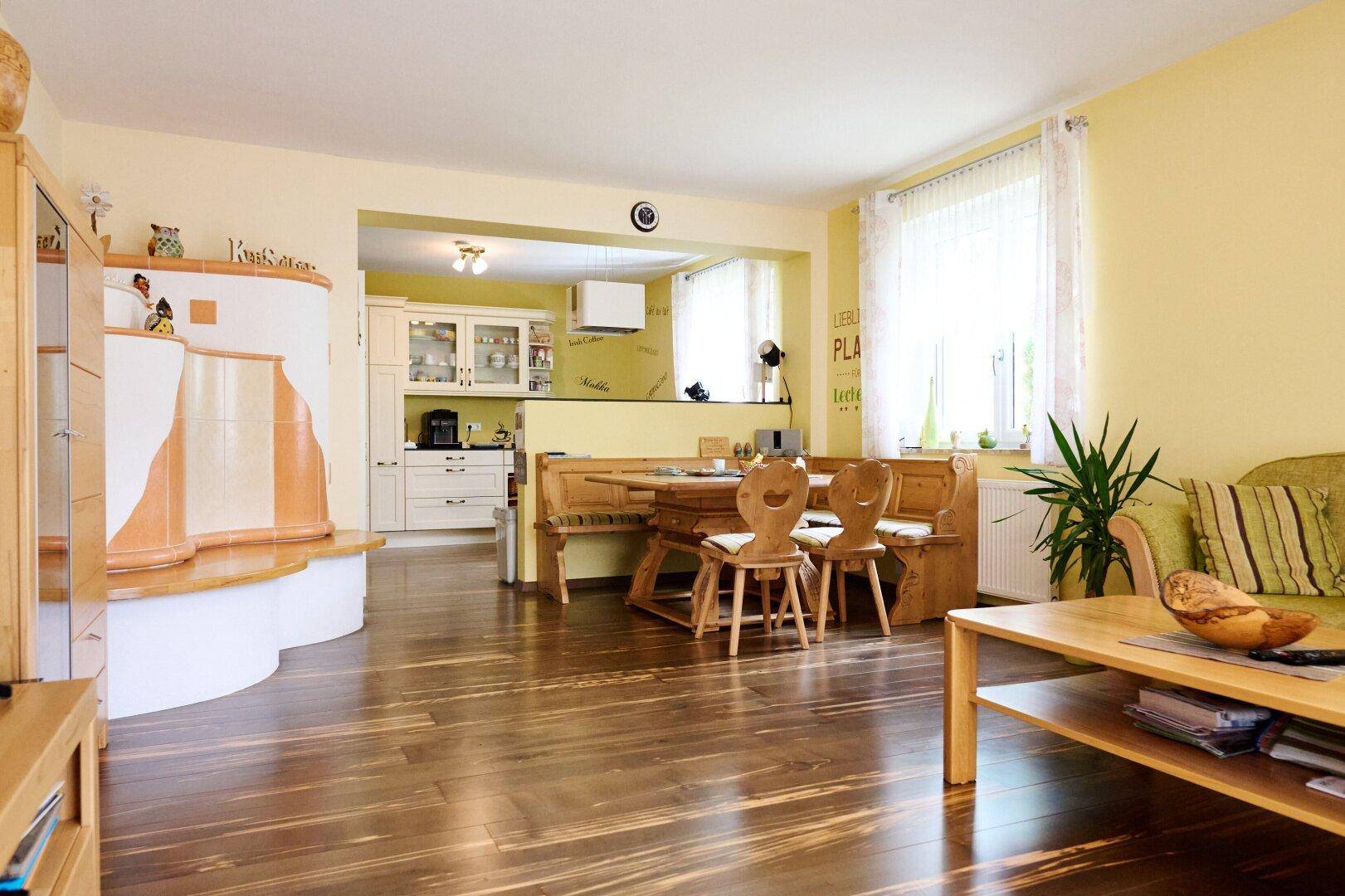 Gemütlicher offener Wohn-Essbereich mit Holzboden, traditionellen Möbeln und Kachelofen.