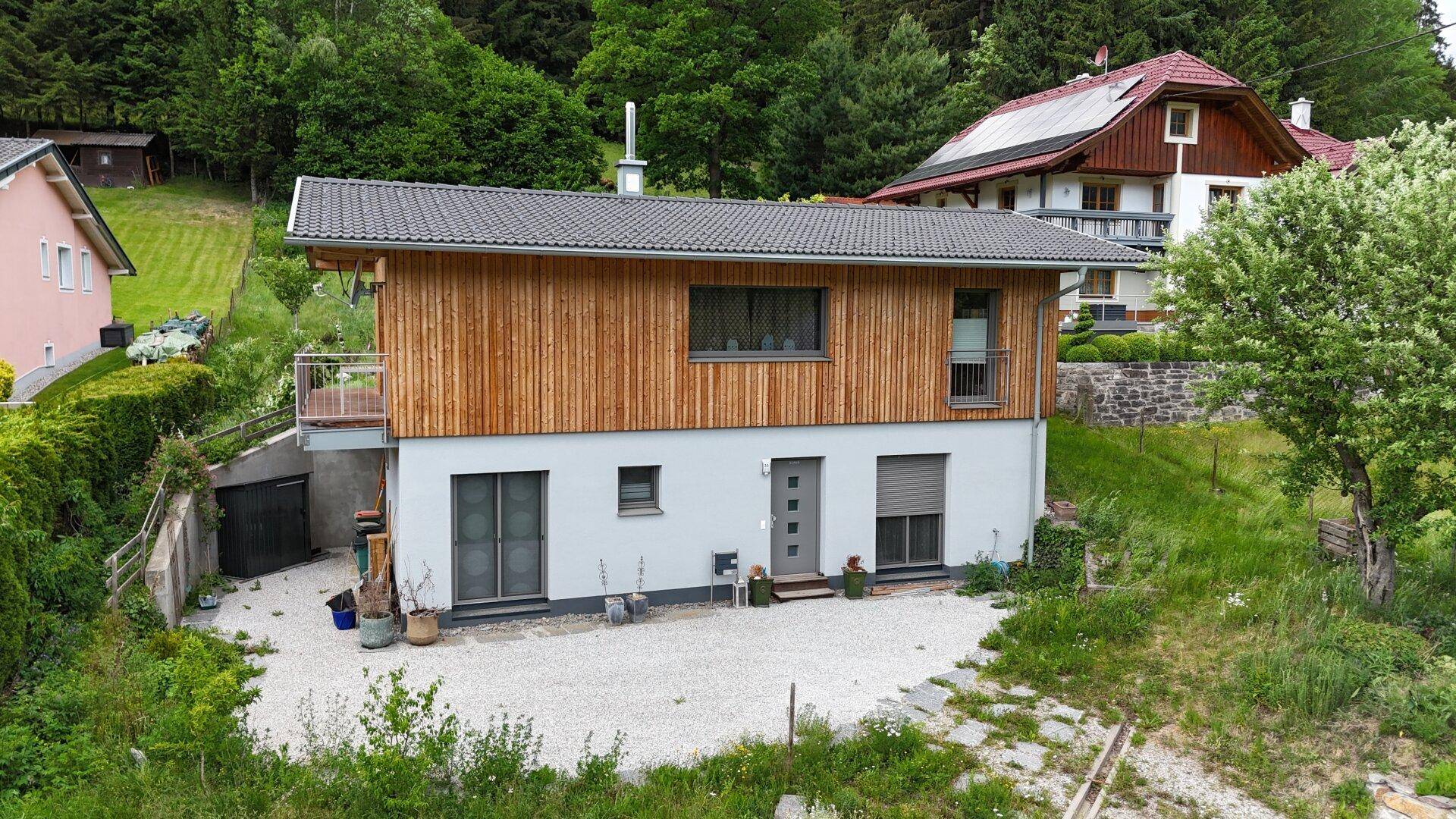 Modernes Haus mit Holzfassade, Balkon und gepflegtem Vorgartenbereich.