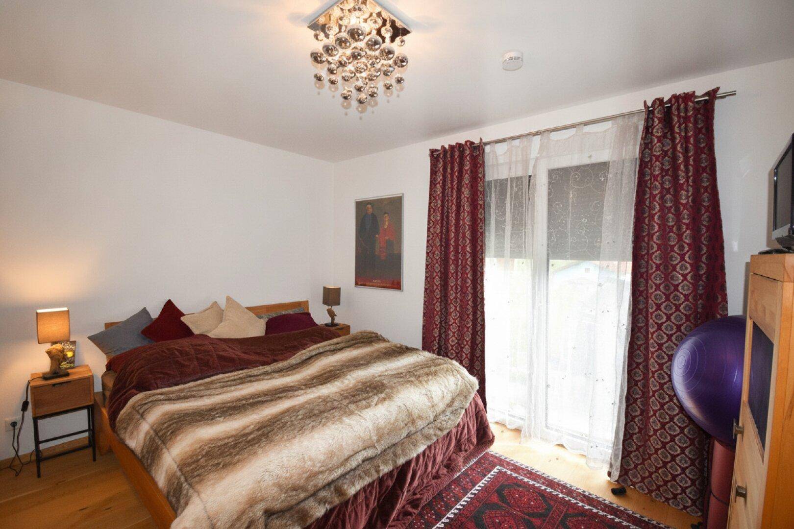 Gemütliches Schlafzimmer mit Doppelbett, Holzboden und Zugang zum Balkon.