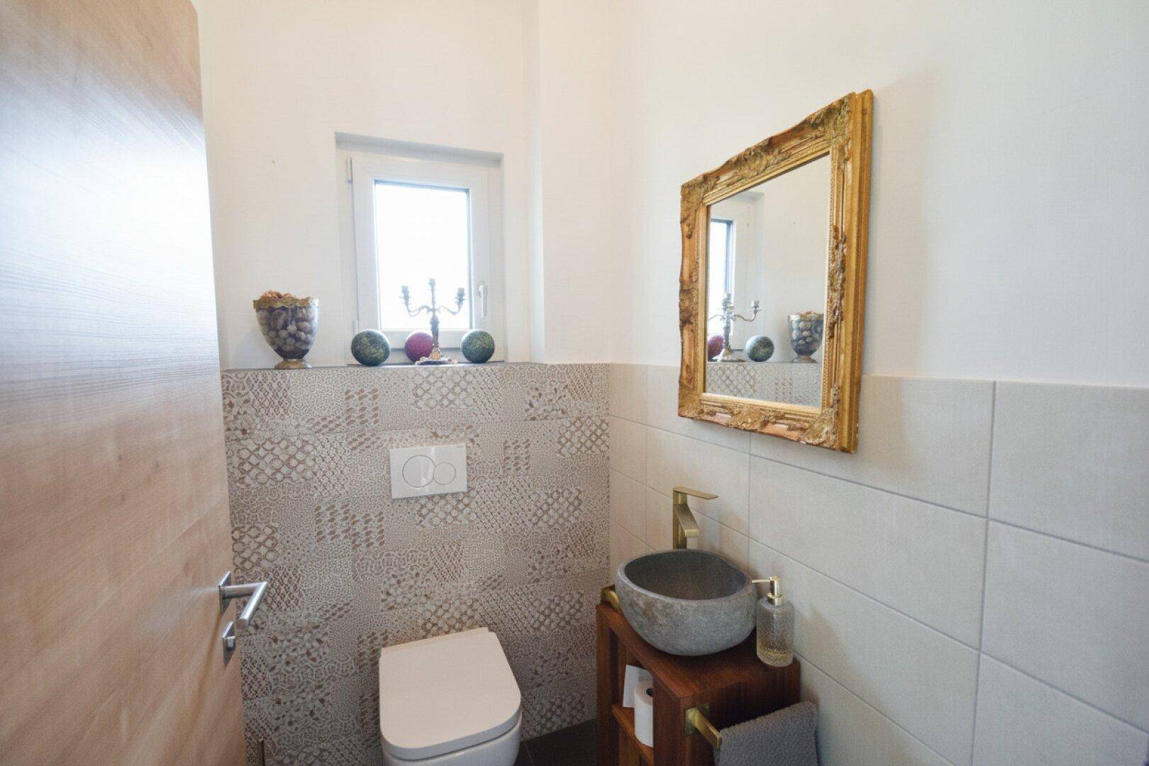 Gäste-WC mit modernem Waschbecken, Wand-WC und dekorativem Spiegel.