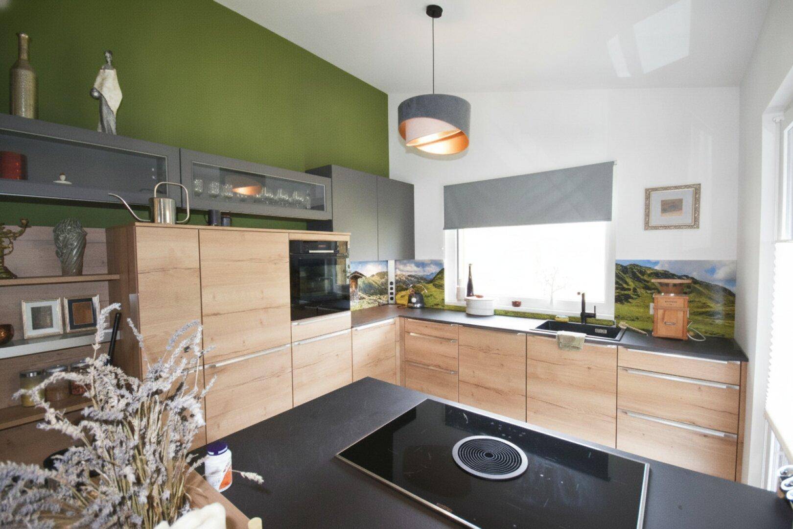 Moderne Küche mit Holzfronten, grüner Akzentwand und Induktionskochfeld.