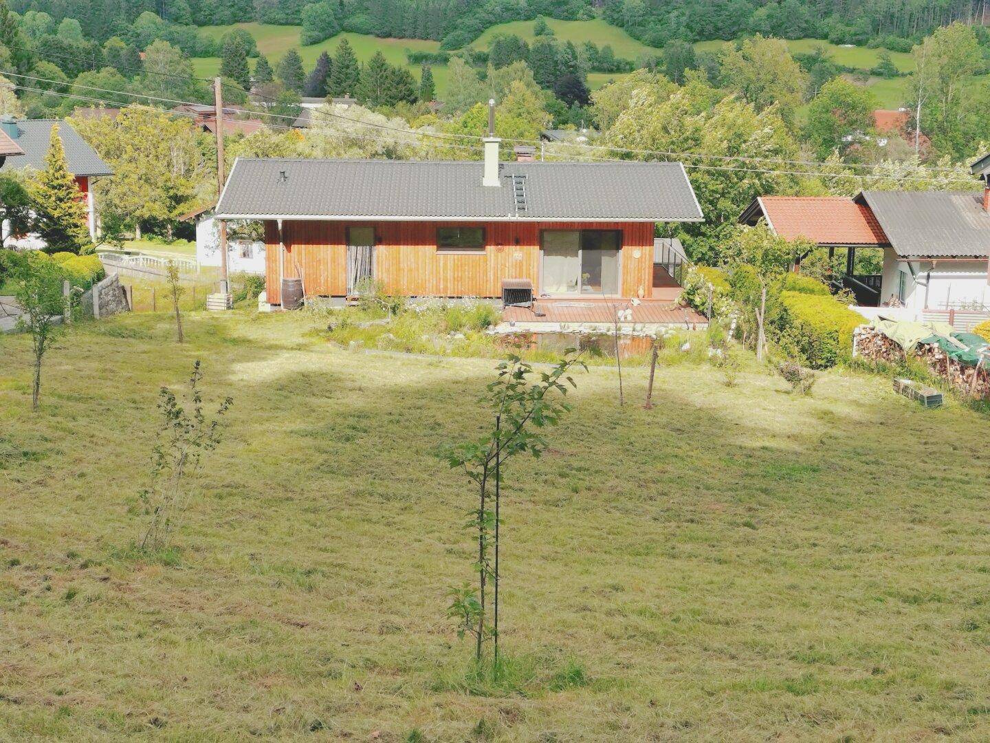 Weitläufige Ansicht des Hauses mit Holzfassade und Naturteich in ländlicher Umgebung.