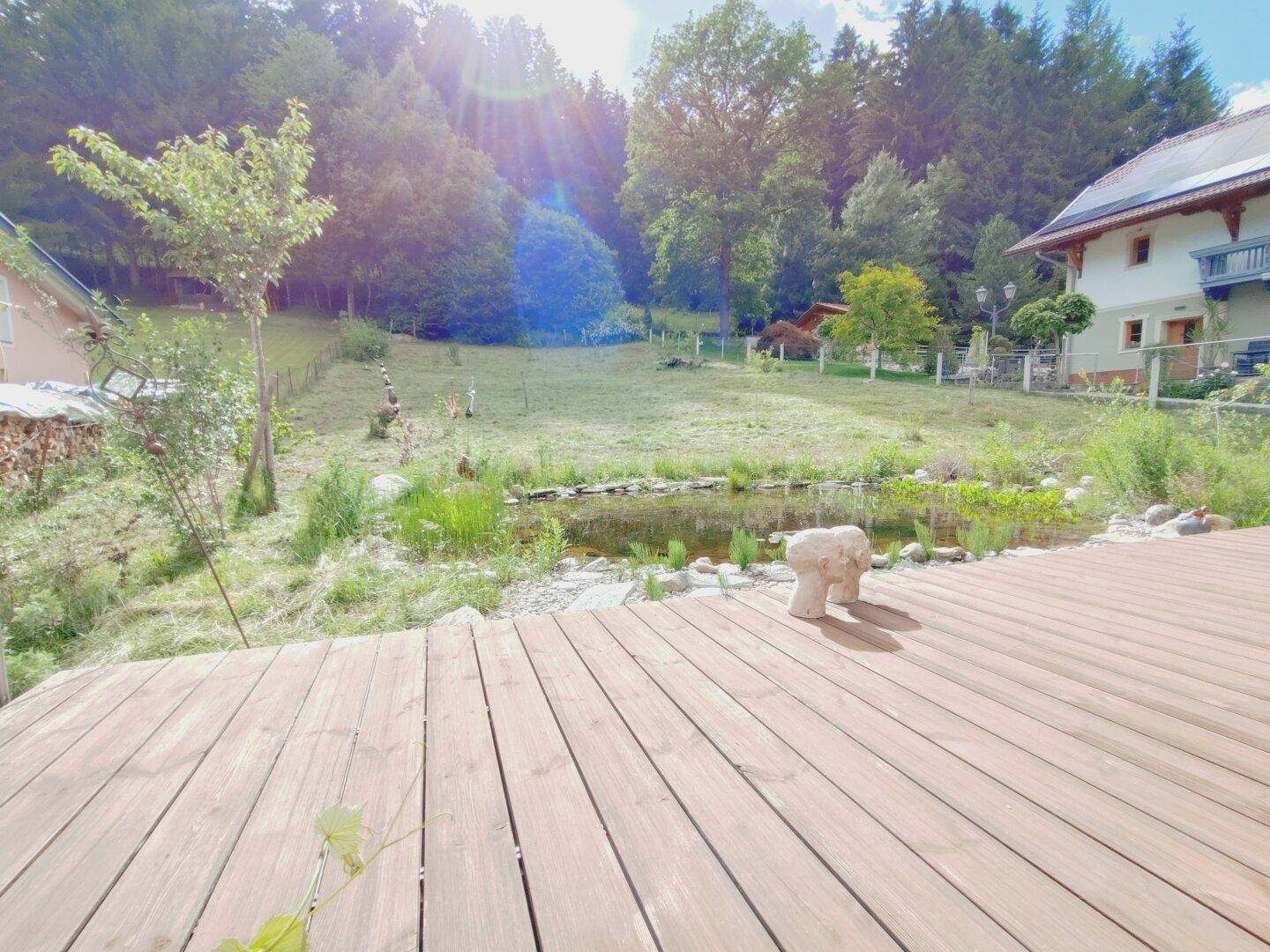 Sonniger Terrassenbereich mit Holzdeck, Naturteich und Blick ins Grüne.