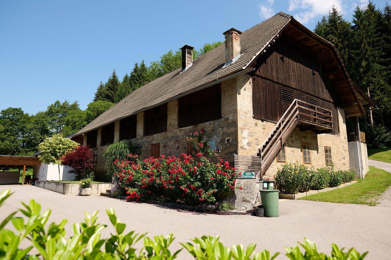 Rustikales Bauernhaus mit Steinfassade, Holzelementen und einem blühenden Rosengarten im Vordergrund.