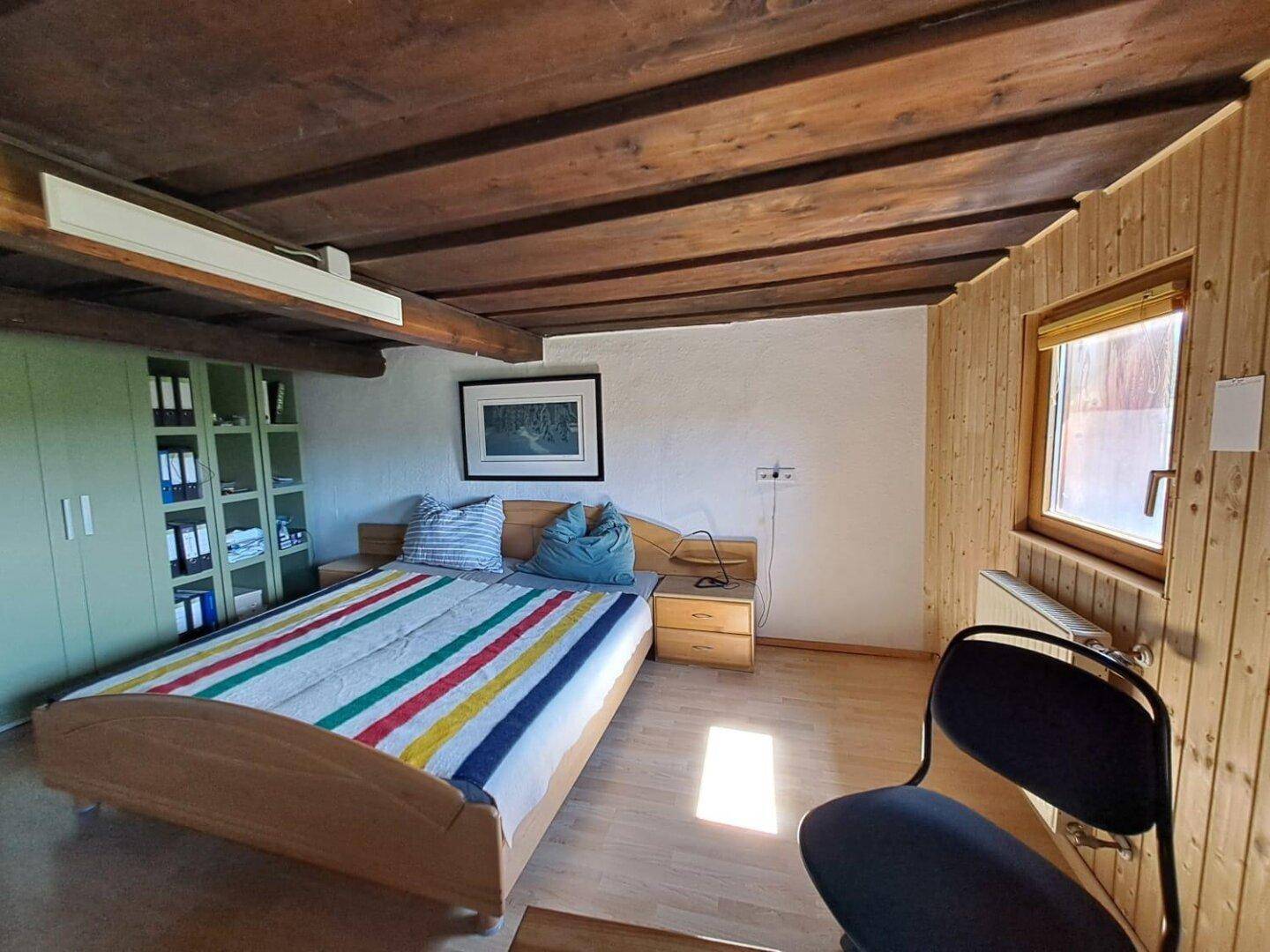 Schlafzimmer mit Holzbalkendecke, Holzvertäfelung und einem Fenster mit natürlichem Lichteinfall.