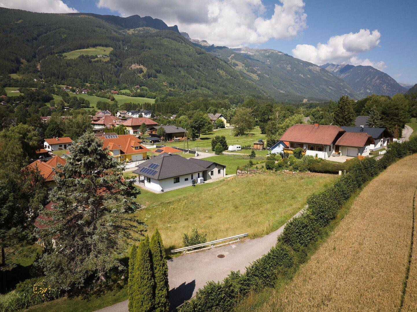 Panoramablick auf ein Wohngebiet mit unbebautem Grundstück und majestätischer Bergkulisse im Hintergrund.