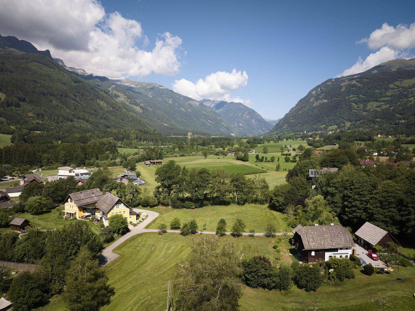 Atemberaubender Panoramablick über ein grünes Tal mit verstreuten Häusern und hohen Bergen.