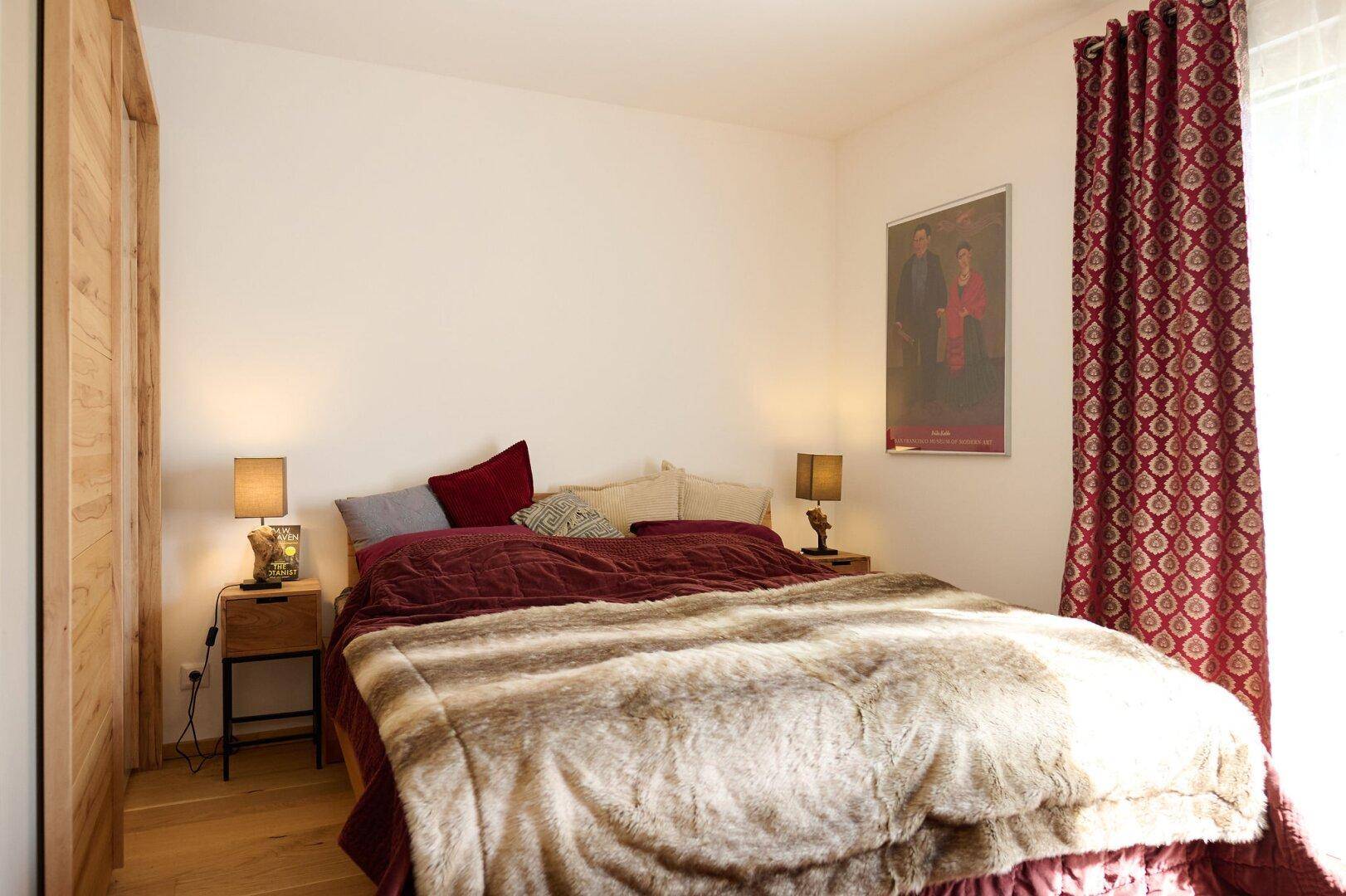 Gemütliches Schlafzimmer mit Doppelbett, Holzboden und roten Vorhängen.