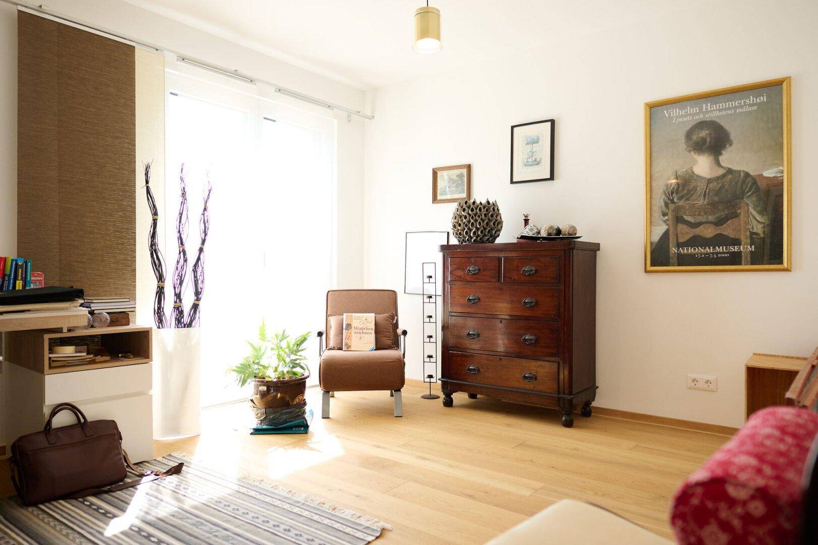 Helles Wohnzimmer mit Holzboden, einem antiken Schrank und großem Fenster.