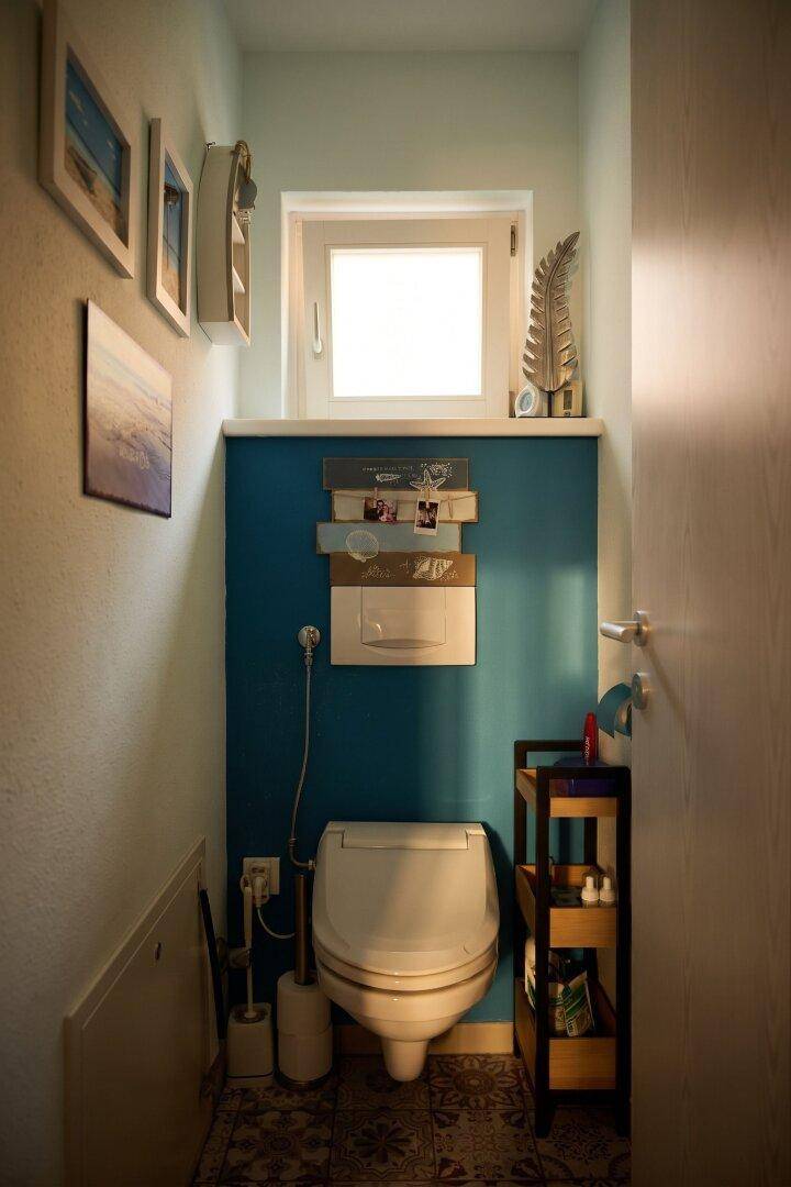 Kleines Gäste-WC mit Fenster, Toilette und blauer Akzentwand.
