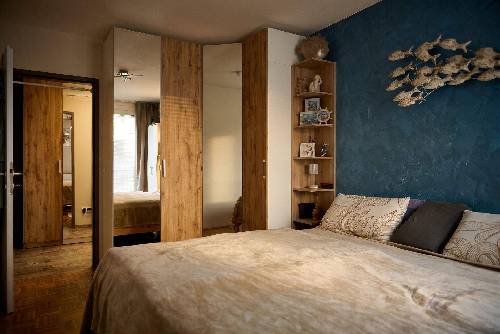 Schlafzimmer mit großem Bett, Spiegelschränken und einer blauen Akzentwand.