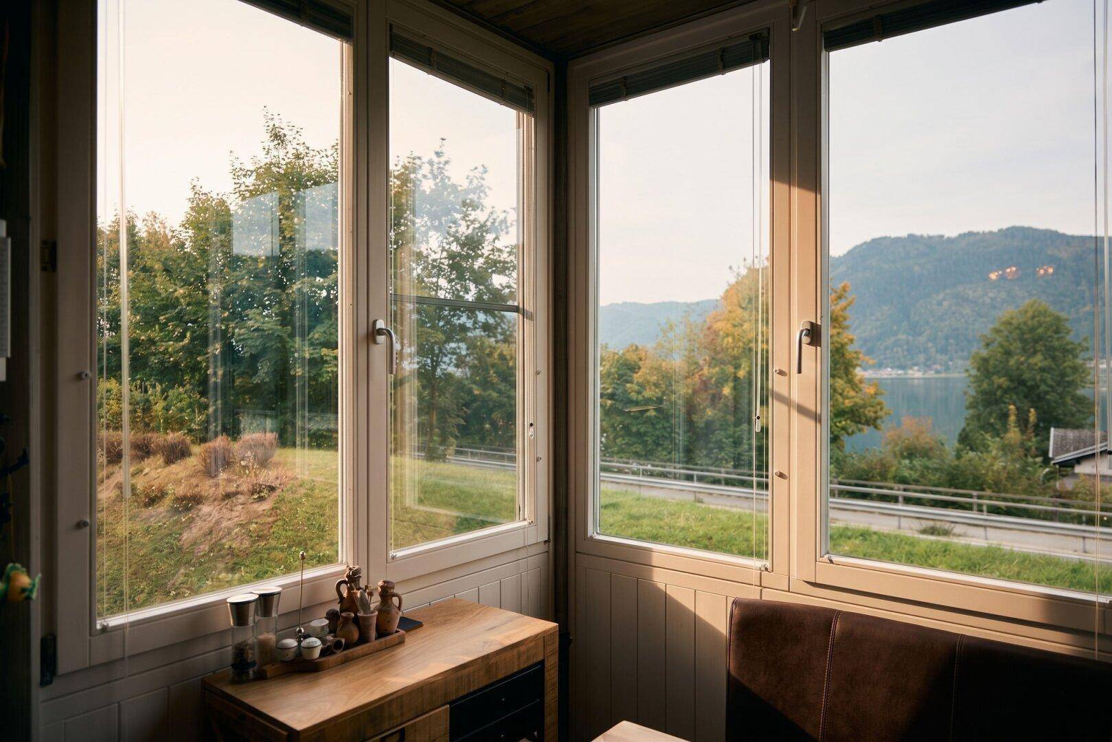 Heller Wintergarten mit großen Fenstern und weitem Blick auf die grüne Landschaft und den See.