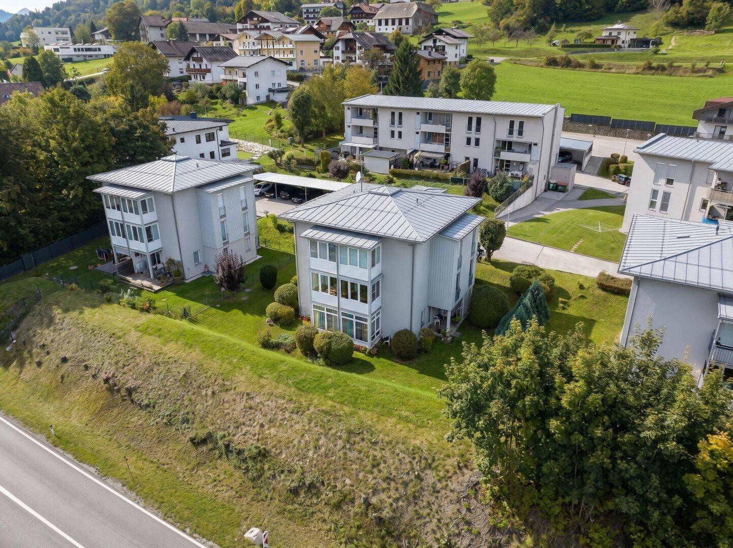 Luftaufnahme von modernen Wohngebäuden in einer grünen Umgebung mit Zufahrtsstraße.
