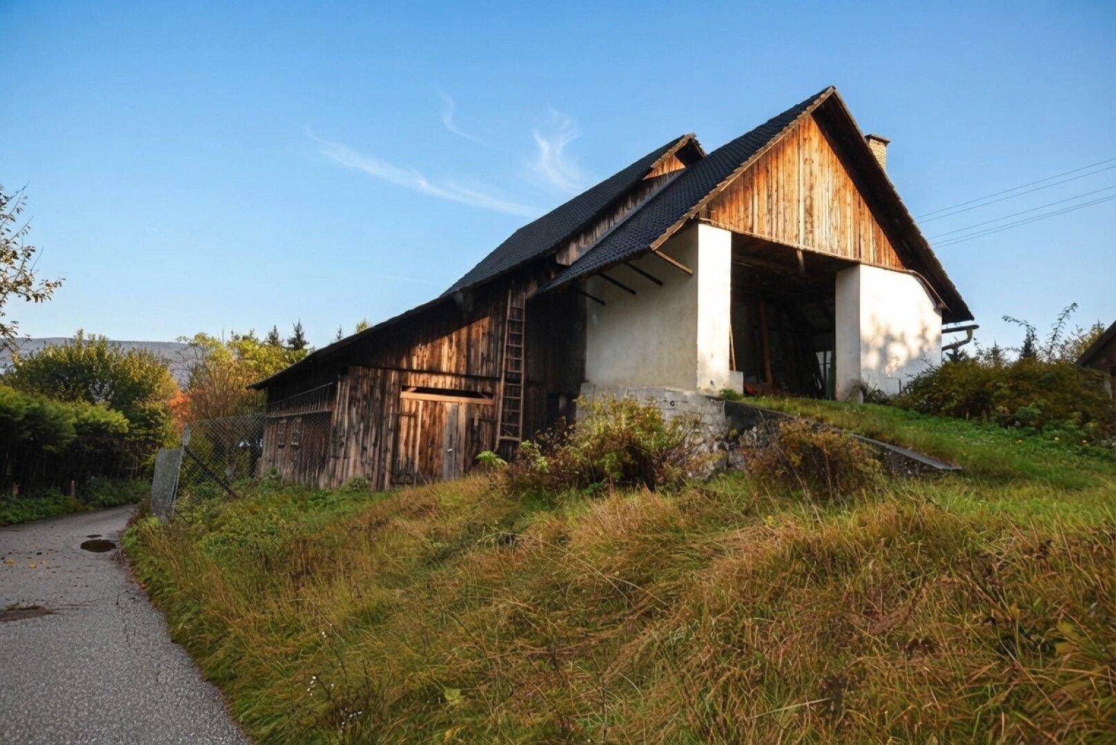 Rustikales Holzgebäude mit dunklem Dach auf einem Grashügel neben einer schmalen Straße.