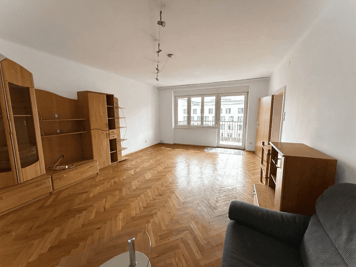 Geräumiges Wohnzimmer mit Fischgrätparkettboden und Zugang zu einem kleinen Balkon.