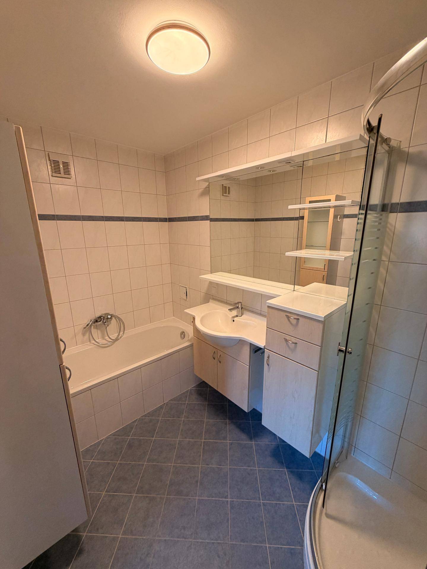 Badezimmer mit Badewanne, Waschbecken und Duschkabine, gefliest in hellen Farben.